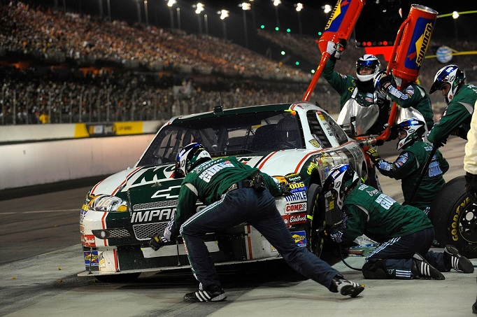 The Pit Crew of a NASCAR driver franticly changes tires and refuels the car