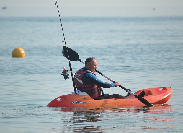 man in his fishing kayak paddling out in the ocean